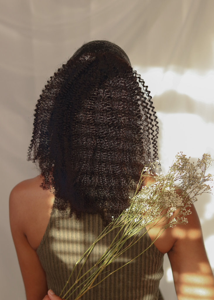 back view of black women wearing 4a 4b drawstring ponytail while holding white dried flowers