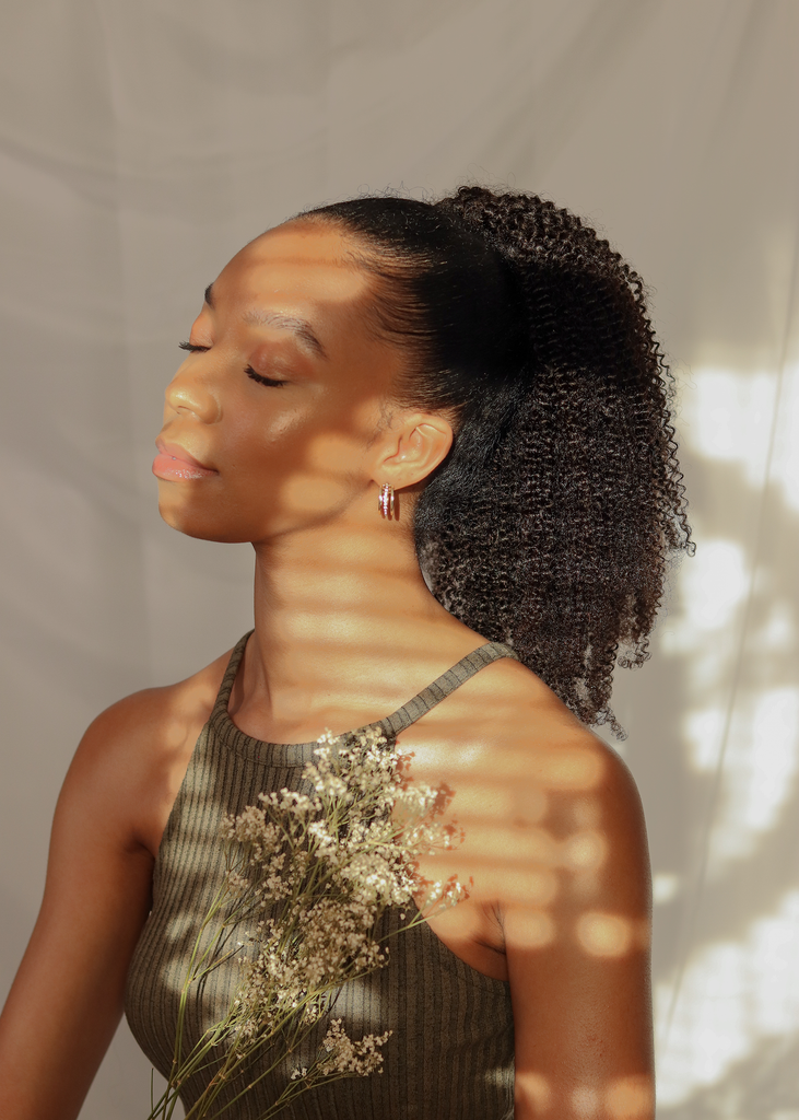 side view of black women wearing 4a 4b ponytail while holding white dried flowers