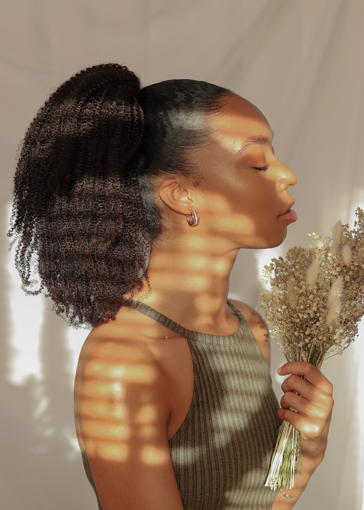 side view of black women wearing an afro ponytail extension while holding white dried flowers